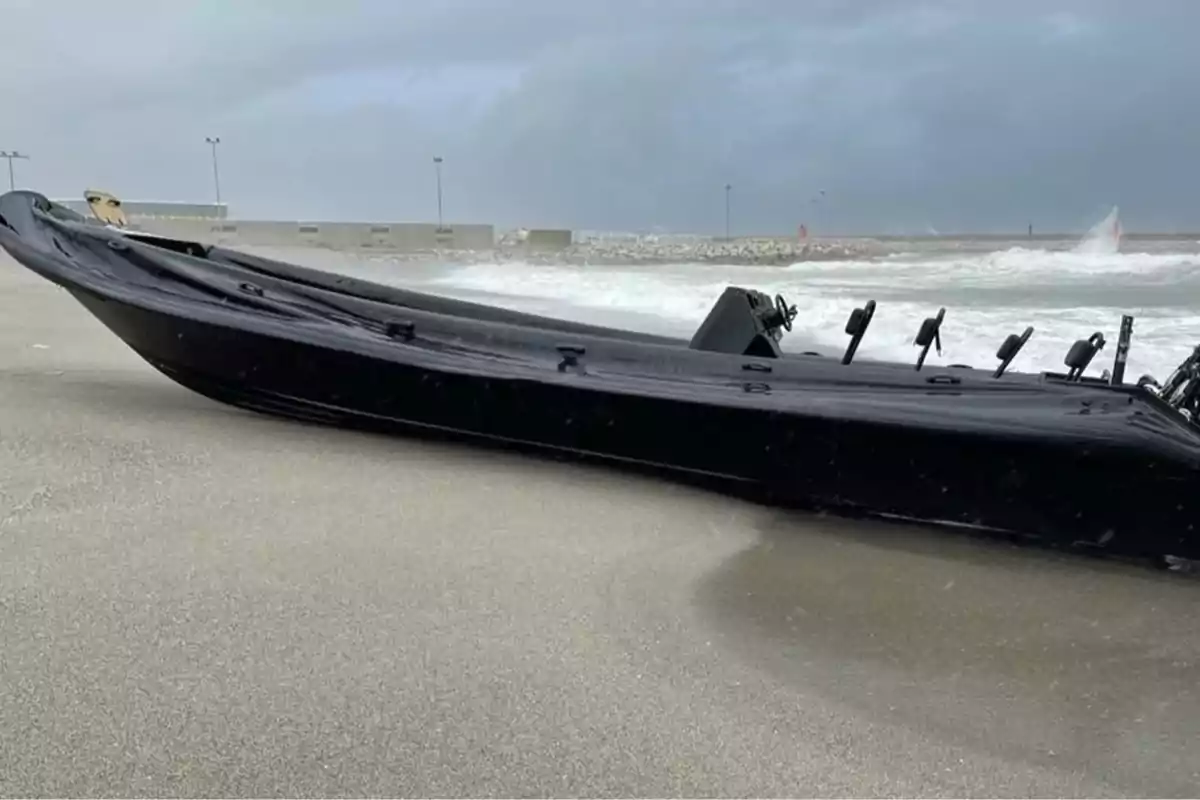 Una lancha negra varada en la arena de una playa con el mar agitado al fondo. Una lancha negra varada en la arena de una playa con el mar agitado al fondo.