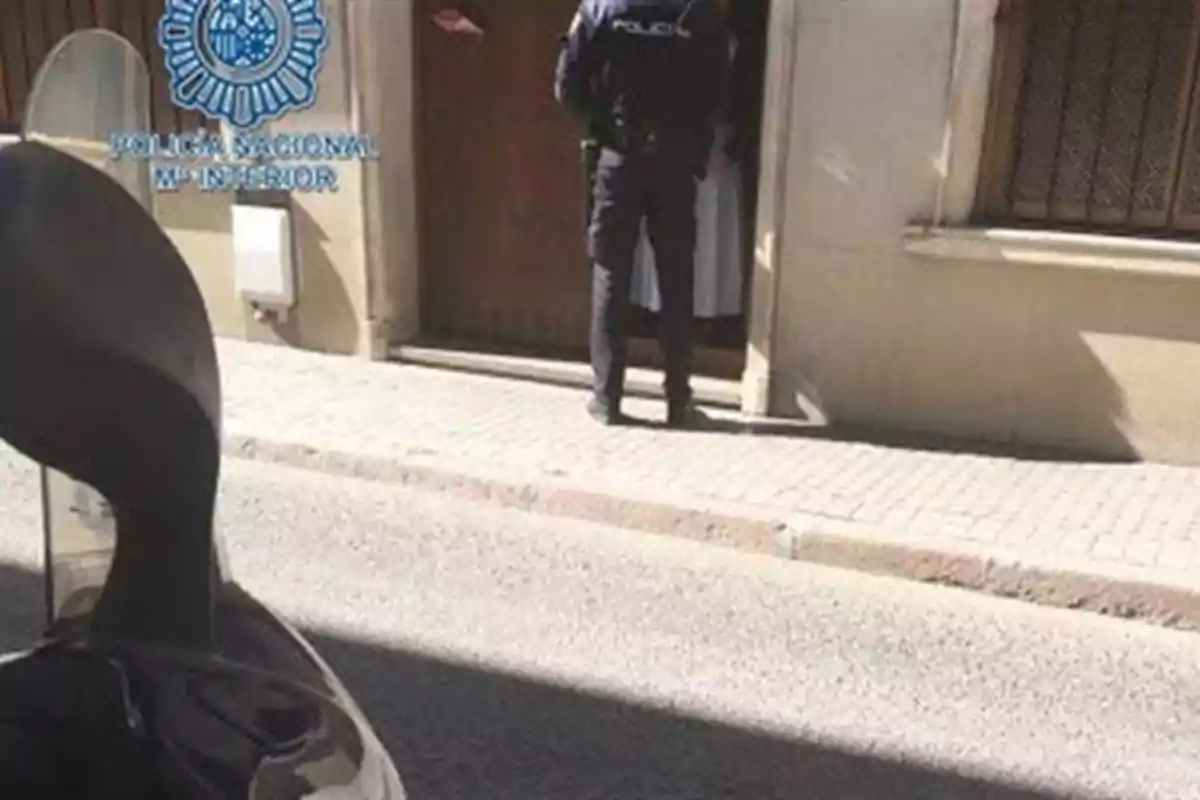 Un policía está de pie frente a una puerta en una calle, con el logotipo de la Policía Nacional visible en la pared.