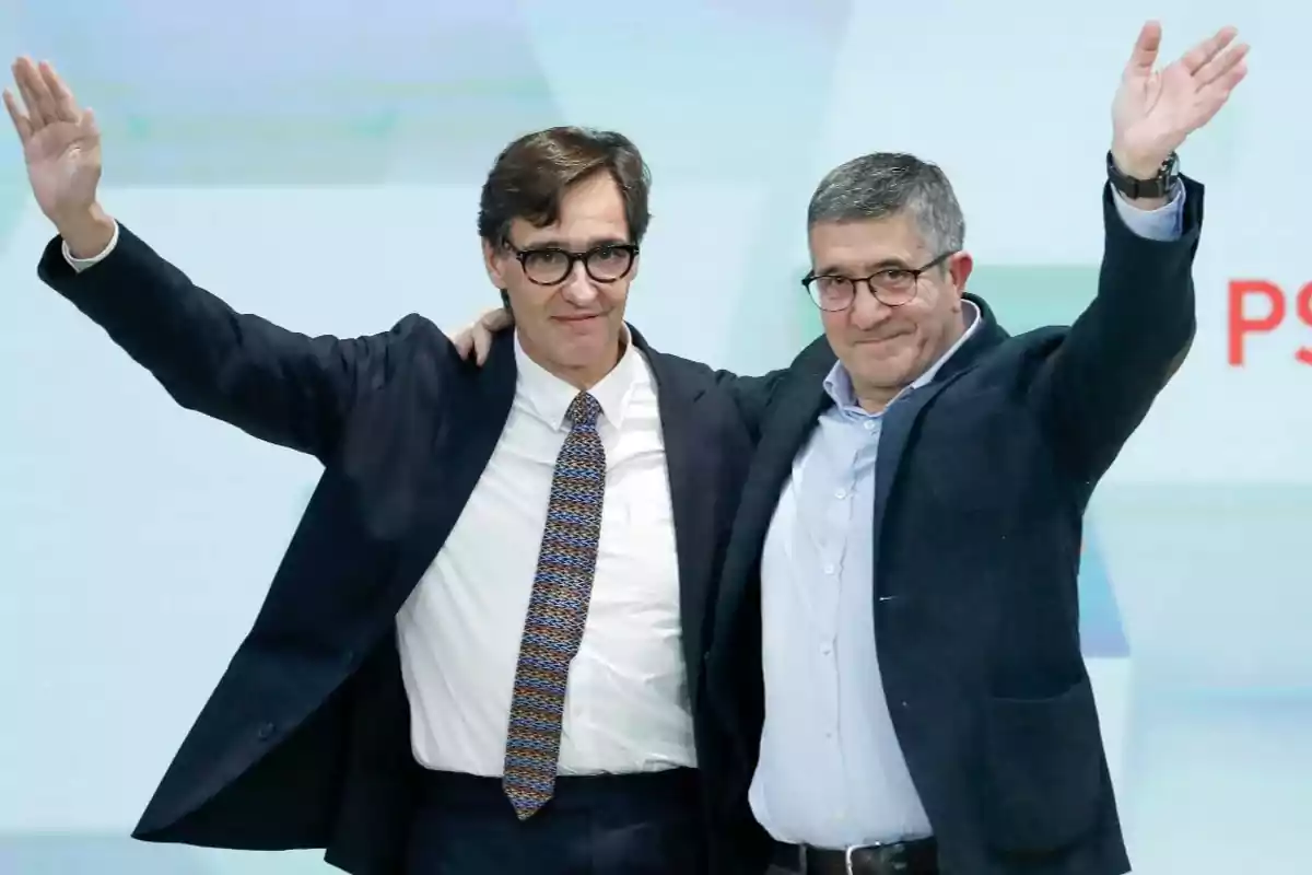 Dos hombres con gafas y traje oscuro sonríen y levantan los brazos mientras posan juntos en un evento Dos hombres con gafas y traje oscuro sonríen y levantan los brazos mientras posan juntos en un evento
