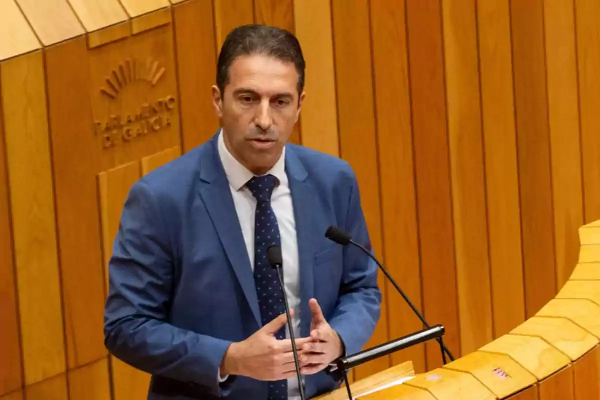 Hombre con traje azul hablando en un atril en el Parlamento de Galicia