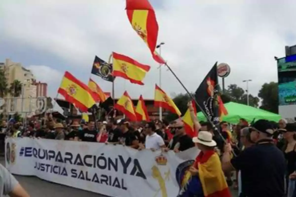 Manifestación con personas ondeando banderas de España y pancarta que dice "Equiparación Ya Justicia Salarial"