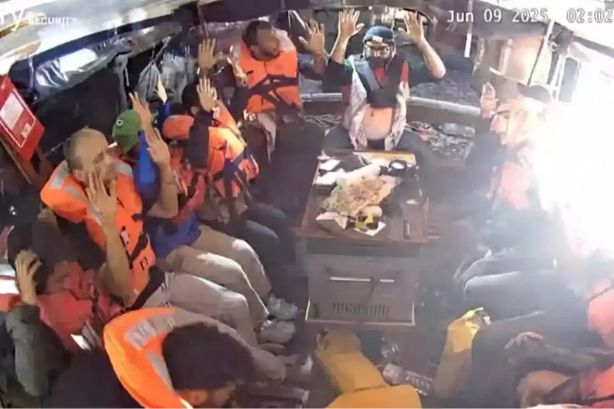Personas con chalecos salvavidas naranjas levantan las manos dentro de una embarcación mientras una luz intensa entra por la derecha Personas con chalecos salvavidas naranjas levantan las manos dentro de una embarcación mientras una luz intensa entra por la derecha