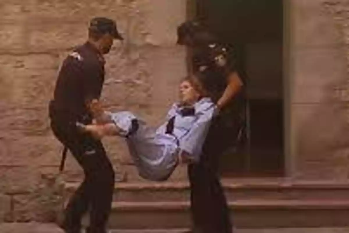 Dos policías llevan a una persona en brazos frente a un edificio de piedra.
