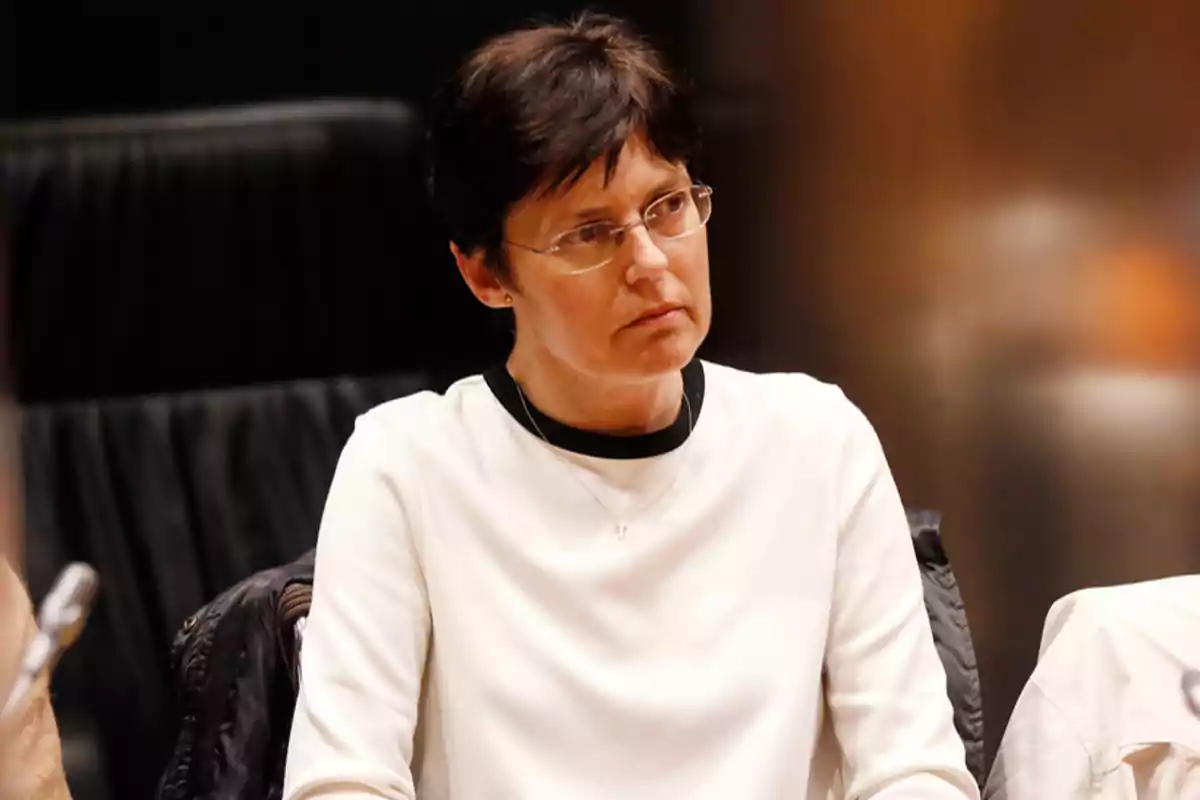 Mujer de cabello corto y oscuro con gafas y suéter blanco sentada en una silla mirando hacia un lado Mujer de cabello corto y oscuro con gafas y suéter blanco sentada en una silla mirando hacia un lado