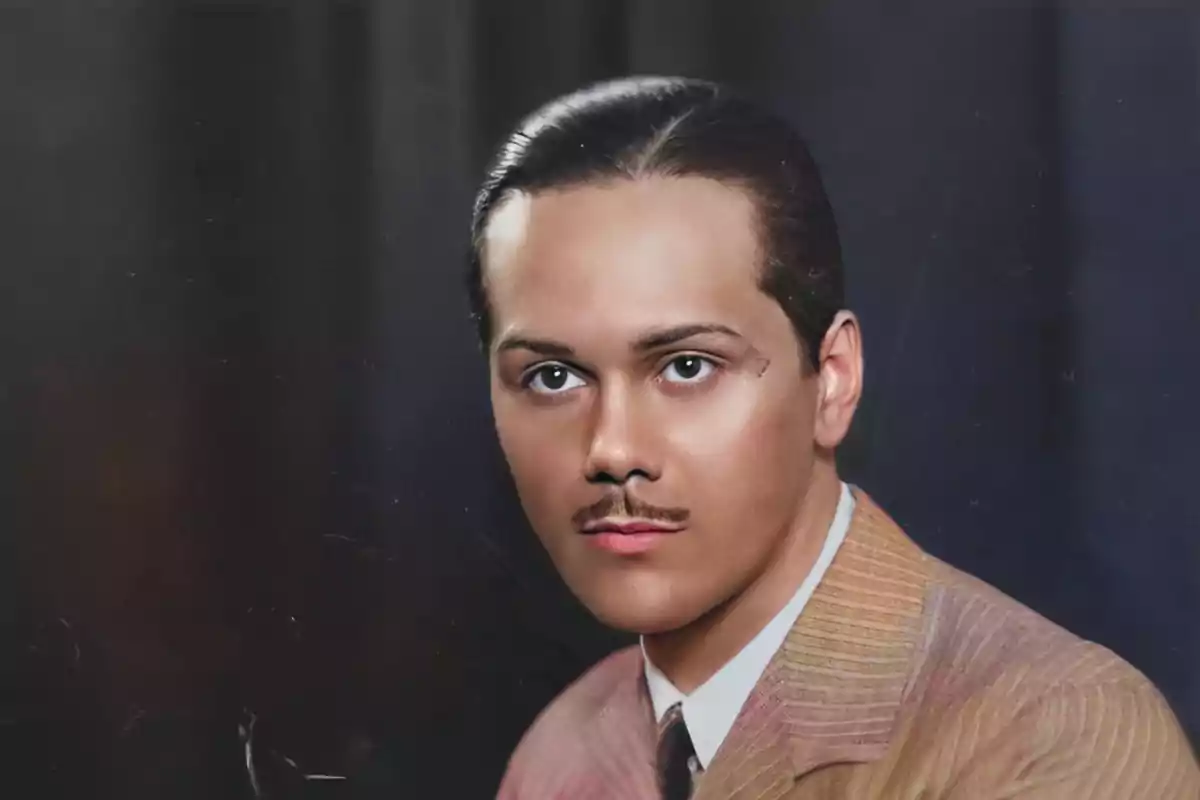 Retrato de un hombre joven con bigote y cabello peinado hacia atrás, vistiendo un traje formal y corbata, con un fondo oscuro.