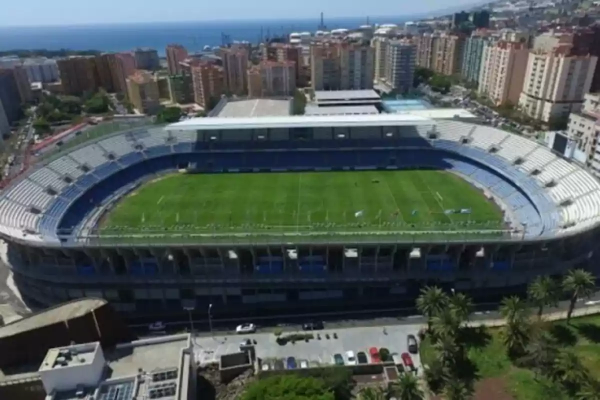 Vista aérea de un estadio de fútbol rodeado de edificios y con el mar al fondo.