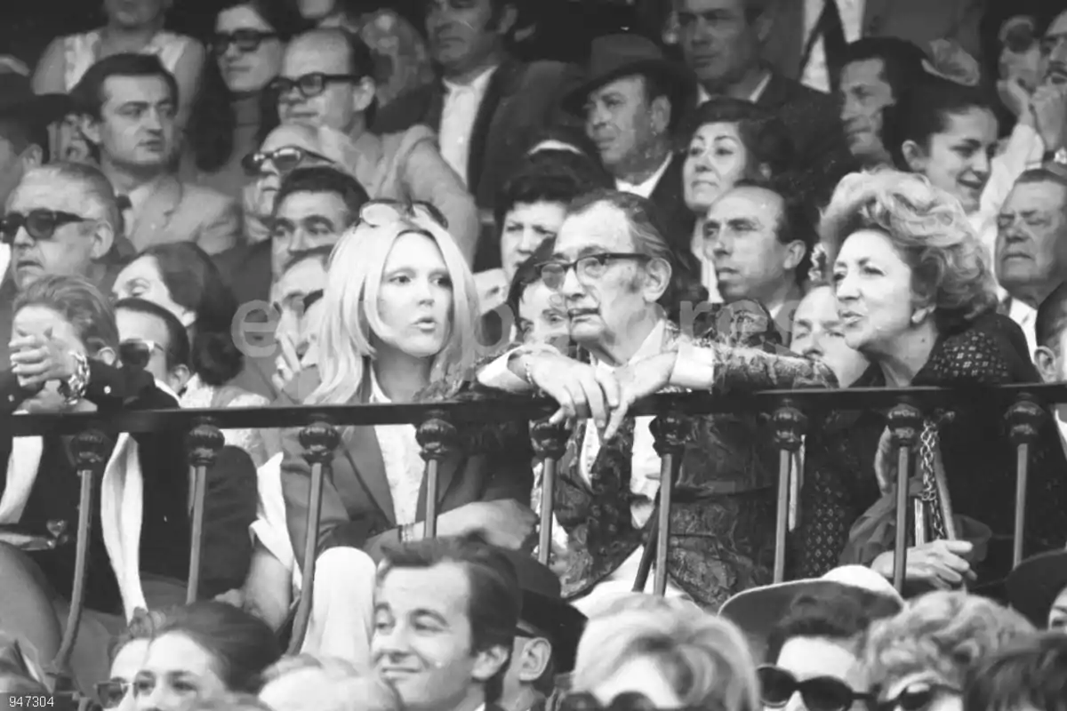 Un grupo de personas sentadas en una grada observando un evento. Un grupo de personas sentadas en una grada observando un evento.