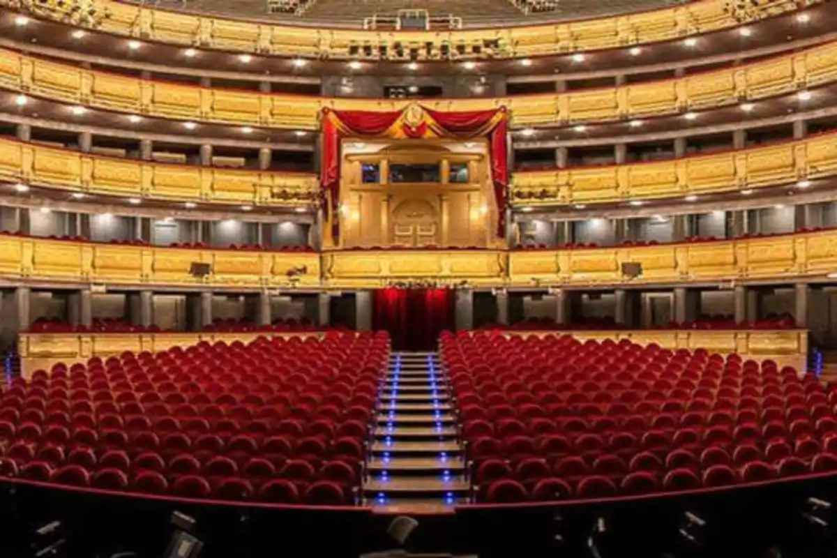 Un teatro con varias filas de asientos rojos y balcones dorados iluminados.