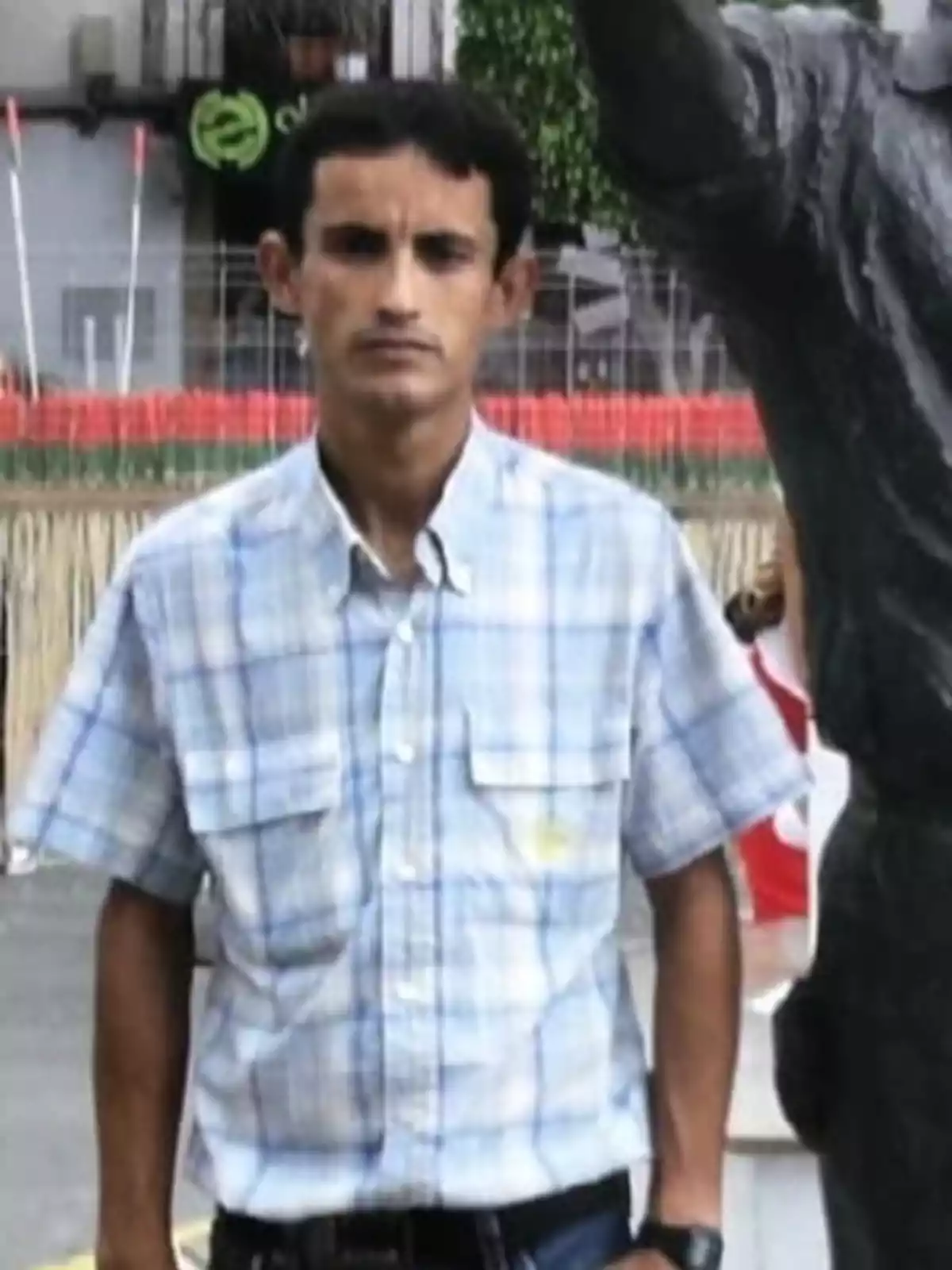 Un hombre con camisa de cuadros de pie junto a una estatua en un entorno urbano.