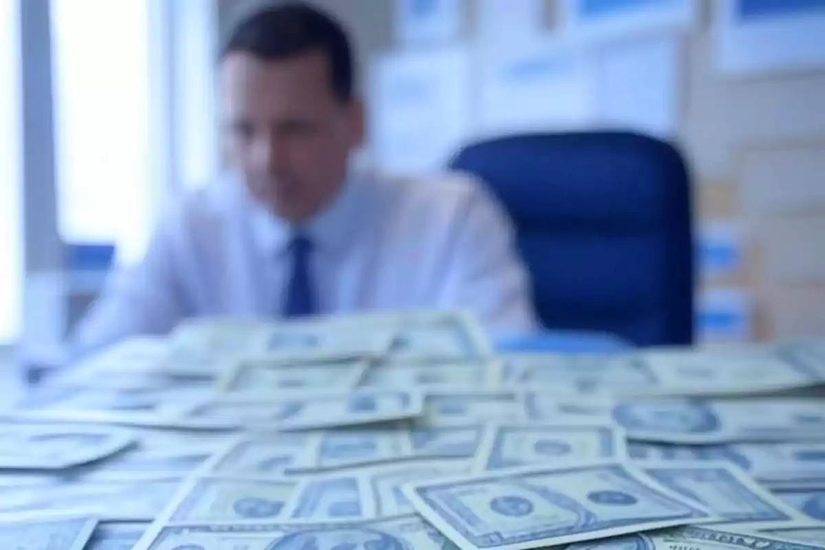 Hombre desenfocado sentado en una oficina con muchos billetes de dólar en primer plano Hombre desenfocado sentado en una oficina con muchos billetes de dólar en primer plano