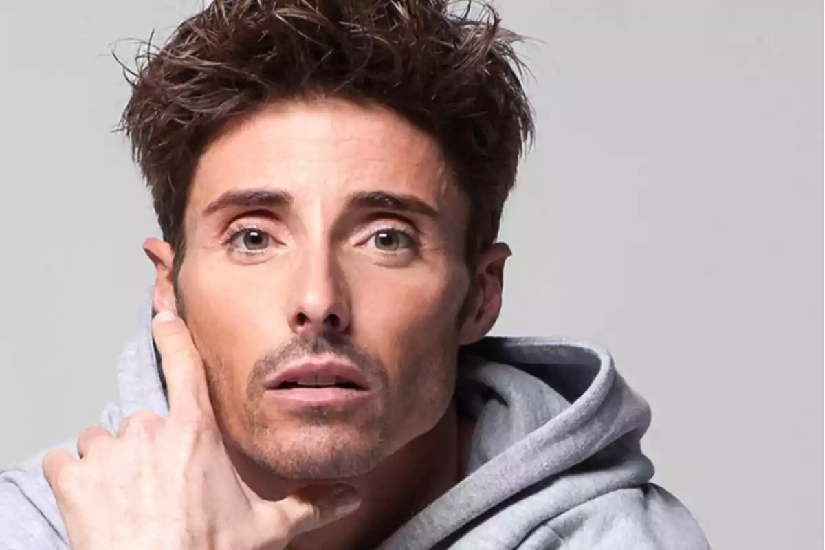 Un hombre con cabello castaño y expresión pensativa lleva una sudadera gris. Un hombre con cabello castaño y expresión pensativa lleva una sudadera gris.