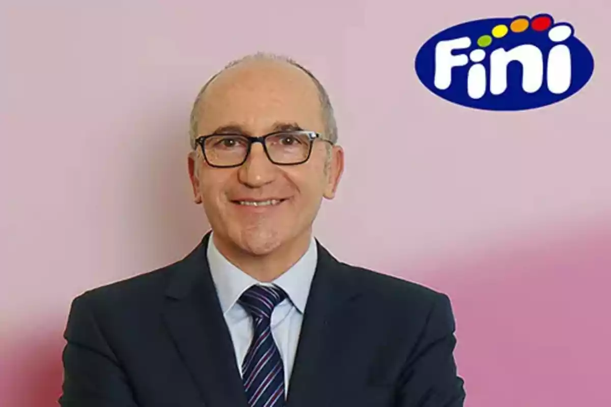 Hombre con gafas y traje oscuro sonriendo frente a un fondo rosa con el logo de Fini en la esquina superior derecha.
