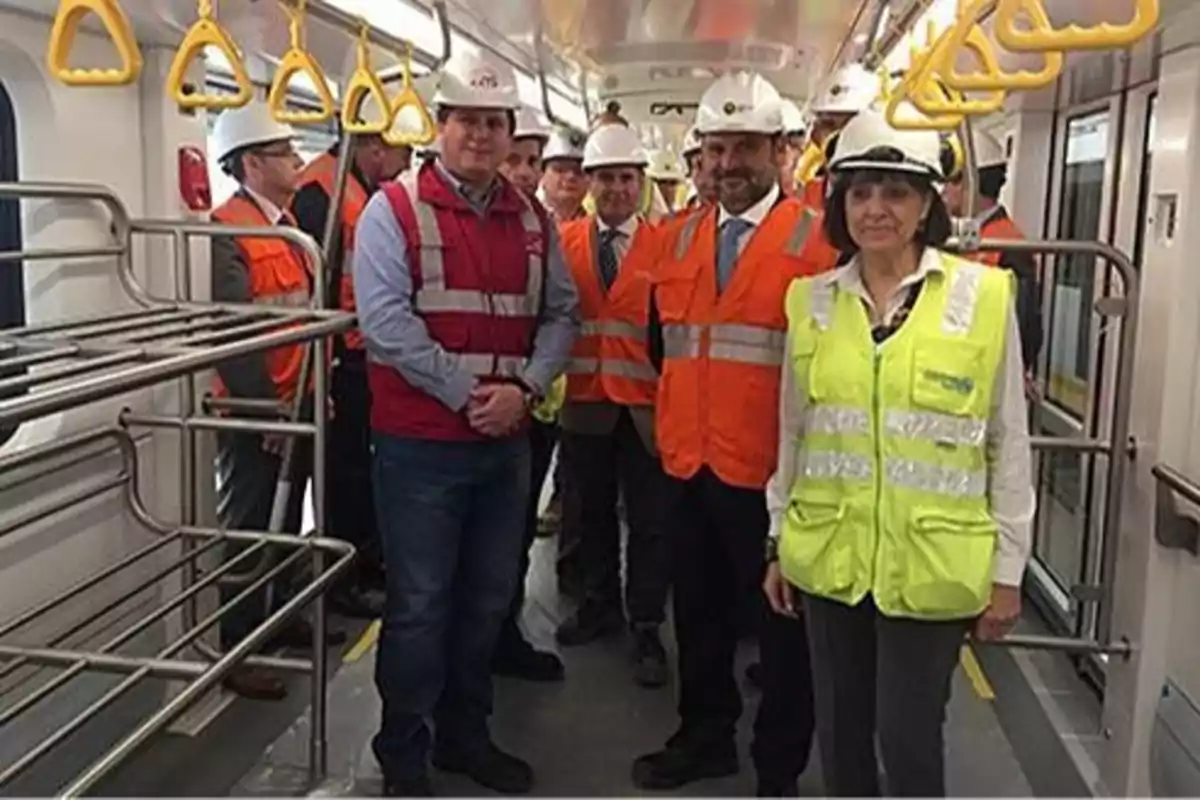 Un grupo de personas con cascos y chalecos de seguridad se encuentra dentro de un vagón de tren en construcción.