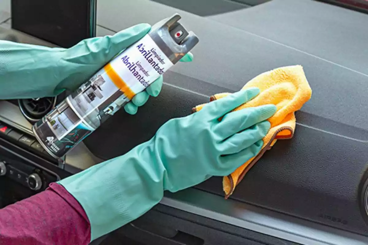 Persona con guantes verdes limpiando el tablero de un auto con un trapo amarillo y un aerosol limpiador Persona con guantes verdes limpiando el tablero de un auto con un trapo amarillo y un aerosol limpiador