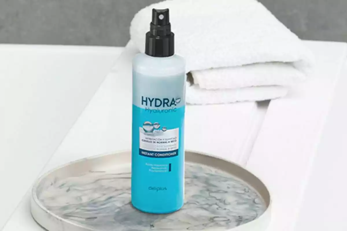 Botella de acondicionador instantáneo Hydra Hyaluronic sobre una bandeja junto a toallas blancas. Botella de acondicionador instantáneo Hydra Hyaluronic sobre una bandeja junto a toallas blancas.