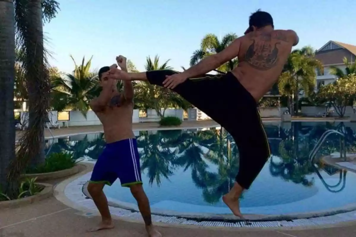 Dos hombres practicando artes marciales junto a una piscina rodeada de palmeras.