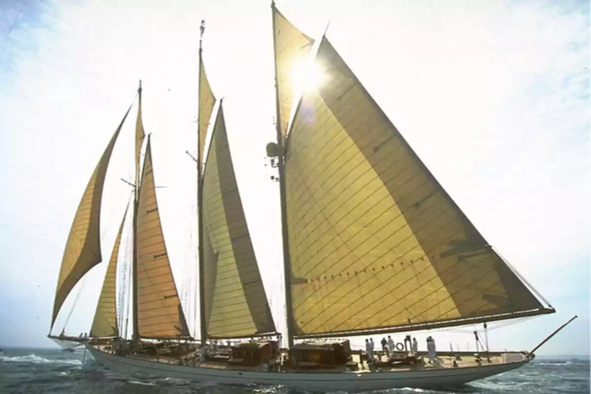 Un velero de tres mástiles navegando en el mar con el sol brillando a través de sus velas.