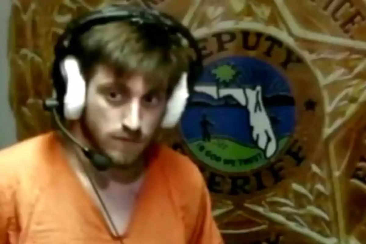 Un hombre con uniforme naranja y auriculares con micrófono frente a un fondo con un escudo de sheriff. Un hombre con uniforme naranja y auriculares con micrófono frente a un fondo con un escudo de sheriff.
