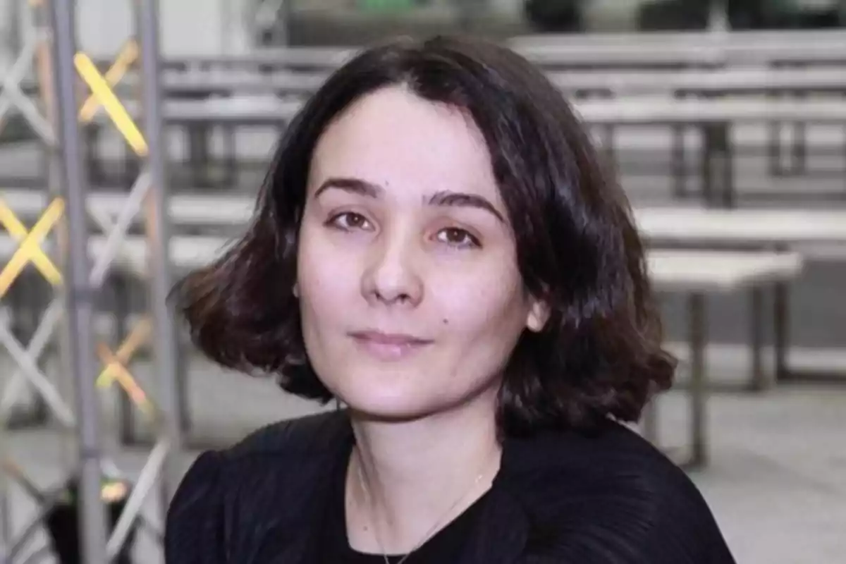 Una persona con cabello oscuro y corto en un entorno interior con estructuras metálicas al fondo. Una persona con cabello oscuro y corto en un entorno interior con estructuras metálicas al fondo.