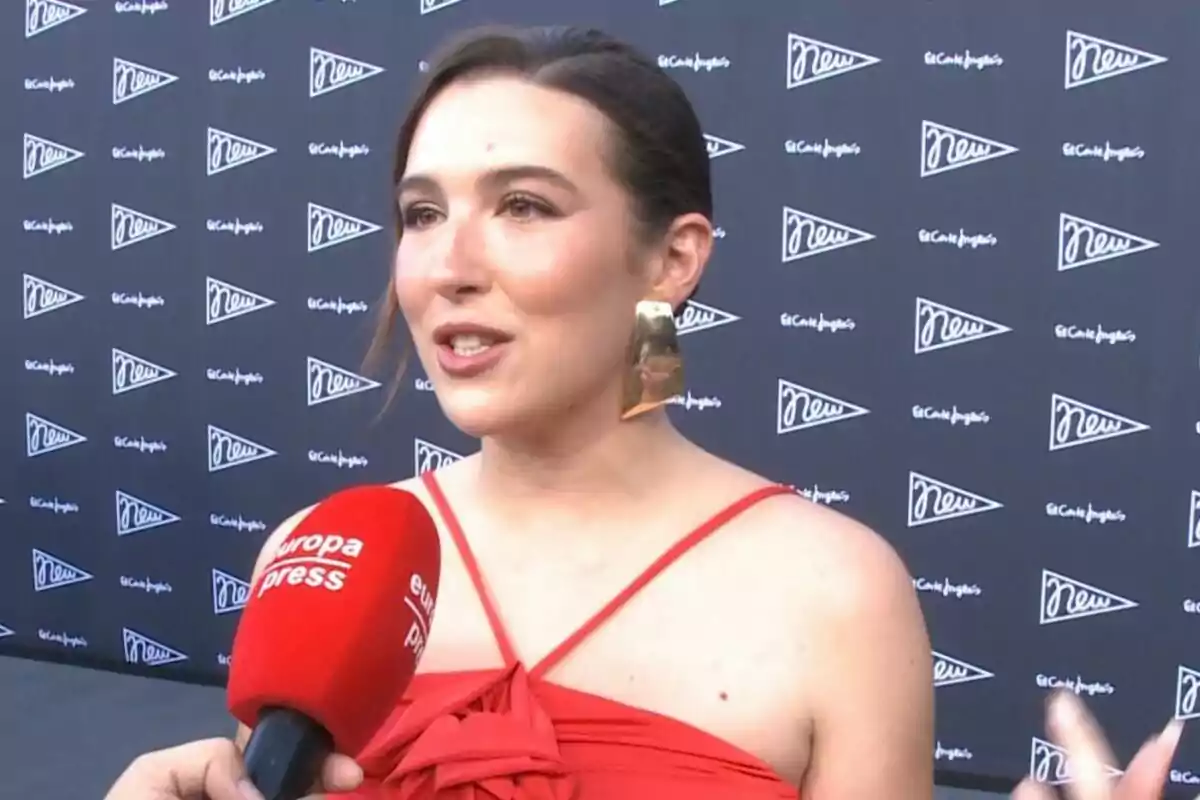 Alba Díaz con vestido rojo siendo entrevistada por un micrófono de Europa Press en un evento con fondo de logotipos de El Corte Inglés. Alba Díaz con vestido rojo siendo entrevistada por un micrófono de Europa Press en un evento con fondo de logotipos de El Corte Inglés.