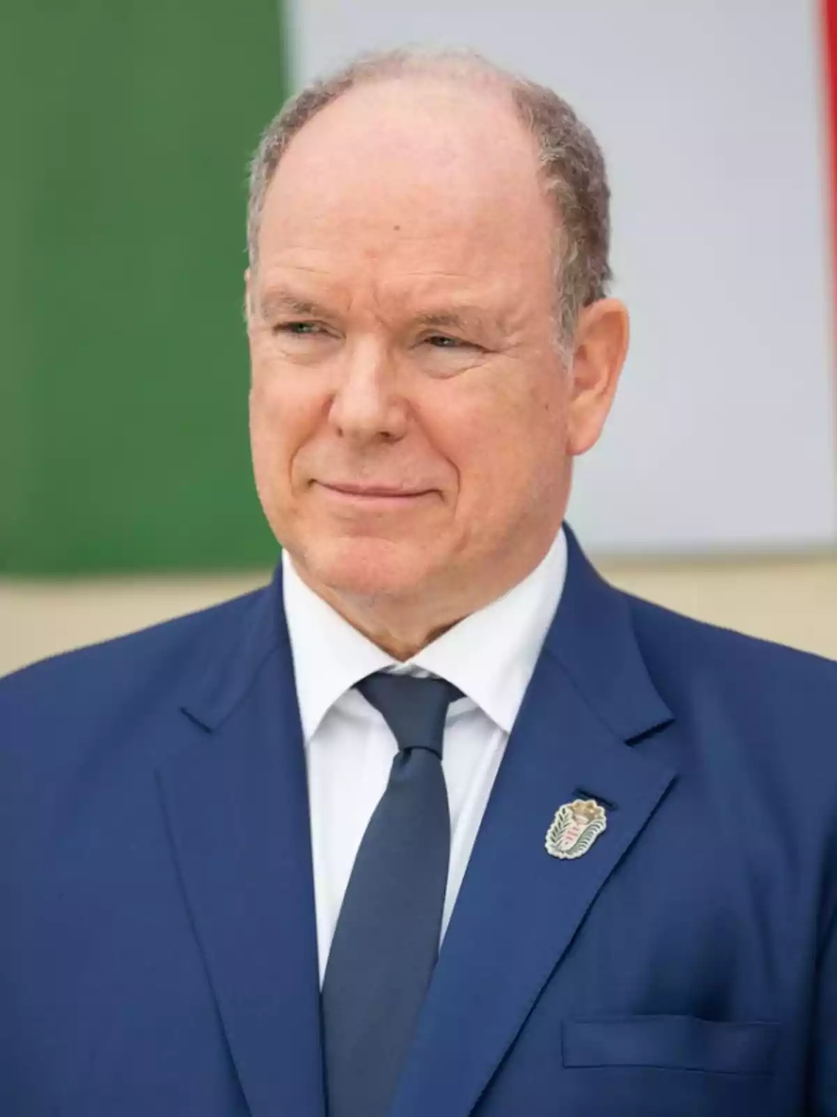 Hombre con traje azul y corbata oscura frente a una bandera. Hombre con traje azul y corbata oscura frente a una bandera.