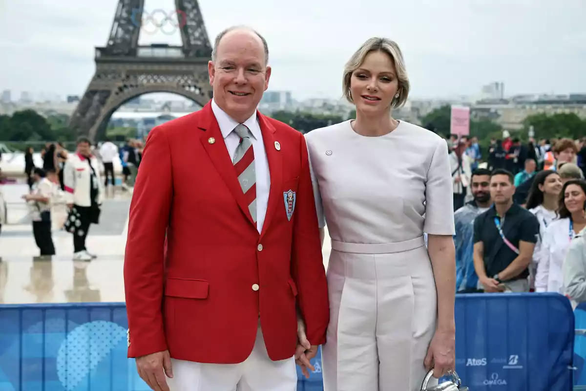 Alberto de Mónaco y Charlene posan frente a la Torre Eiffel, una de ellas lleva un traje rojo y la otra un conjunto blanco, rodeados de un grupo de personas y con un cielo nublado de fondo. Alberto de Mónaco y Charlene posan frente a la Torre Eiffel, una de ellas lleva un traje rojo y la otra un conjunto blanco, rodeados de un grupo de personas y con un cielo nublado de fondo.