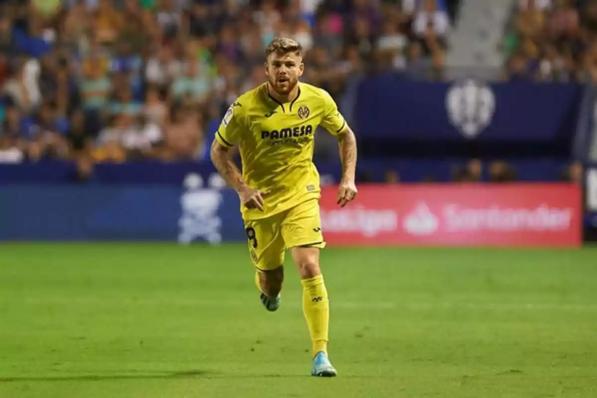Futbolista con uniforme amarillo del Villarreal corriendo en el campo durante un partido con público en las gradas al fondo Futbolista con uniforme amarillo del Villarreal corriendo en el campo durante un partido con público en las gradas al fondo