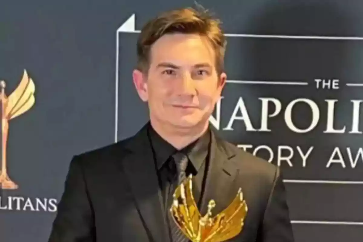 Un hombre con traje oscuro sostiene un trofeo dorado frente a un fondo que dice "Napolitans Story Awards".