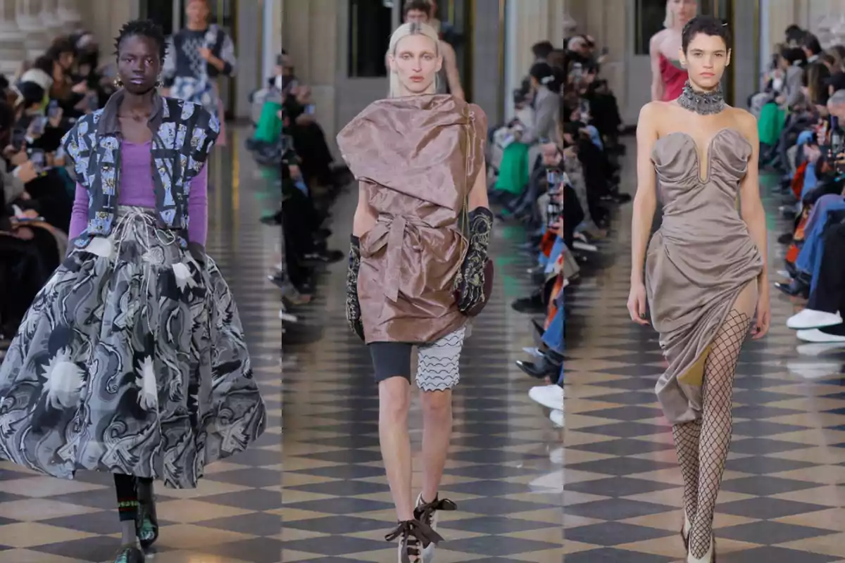 Tres modelos desfilan en una pasarela de moda vistiendo atuendos vanguardistas y originales mientras el público observa desde los costados Tres modelos desfilan en una pasarela de moda vistiendo atuendos vanguardistas y originales mientras el público observa desde los costados