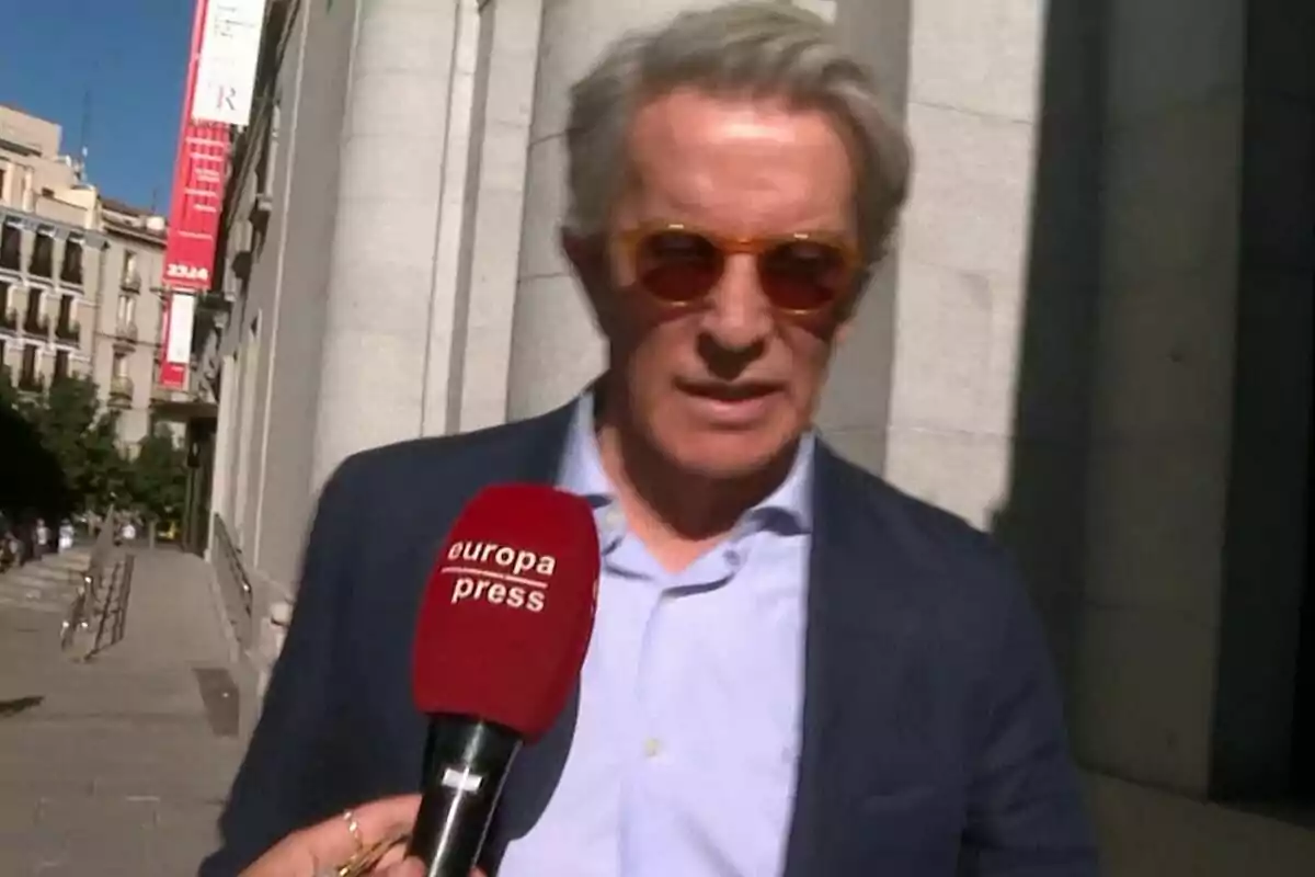Alfonso Díez con gafas de sol y traje azul es entrevistado por un micrófono de Europa Press en una calle urbana.