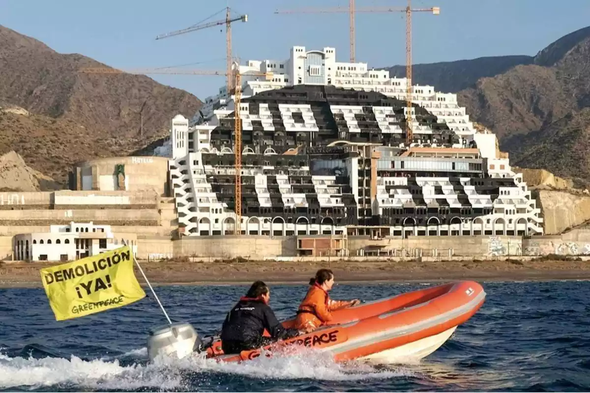 Pintada de "hotel ilegal" en el hotel 'El Algarrobico' y una lancha de Greenpeace observando con dos personas y una bandera amarilla de "demolición ¡ya!", observando la construcción desde el mar.
