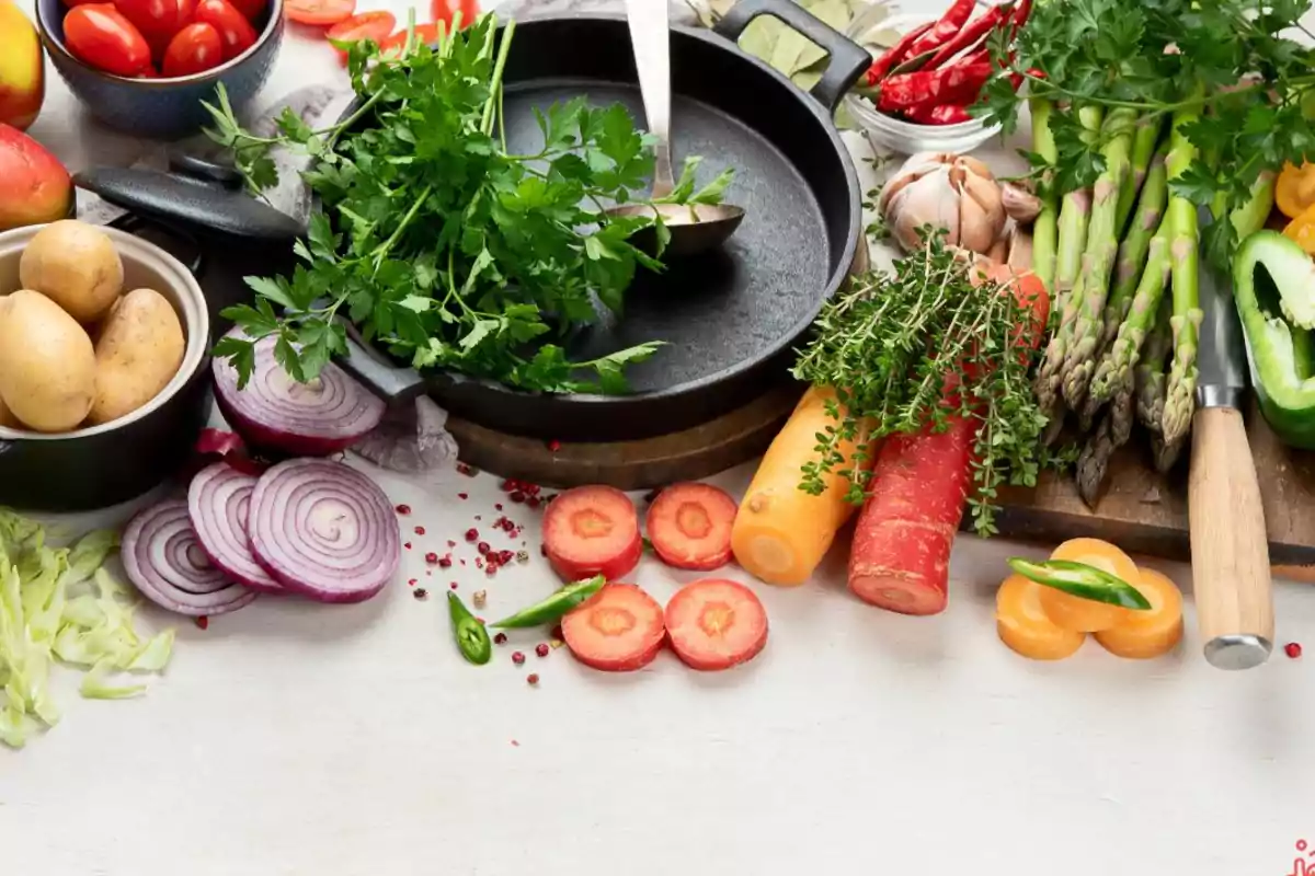 Una variedad de verduras frescas y hierbas alrededor de una sartén de hierro fundido.