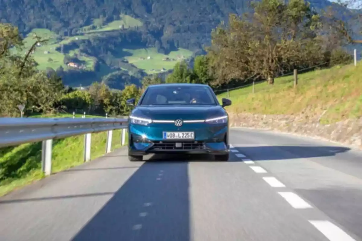 Un coche Volkswagen ID.7 Pro S azul oscuro circula por una carretera rodeada de un paisaje montañoso y verde.