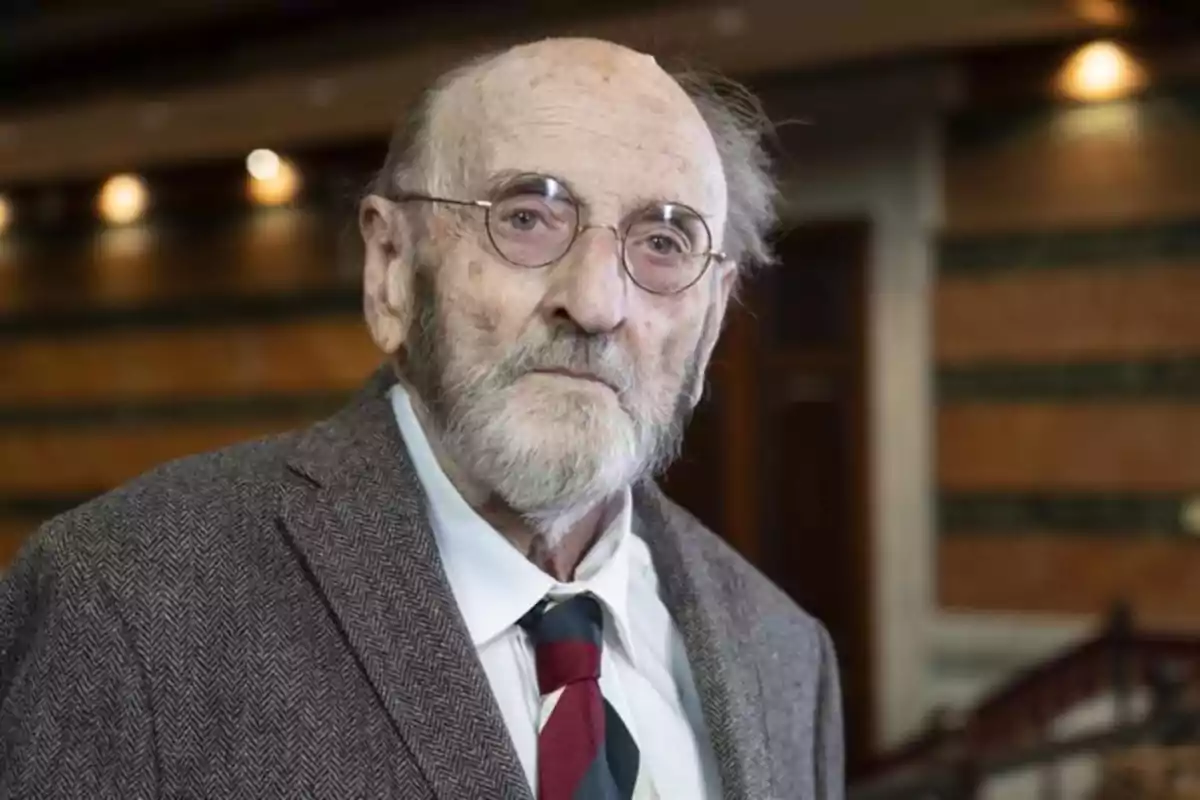 Un hombre mayor con barba y gafas, vestido con traje y corbata, en un entorno interior elegante. Un hombre mayor con barba y gafas, vestido con traje y corbata, en un entorno interior elegante.