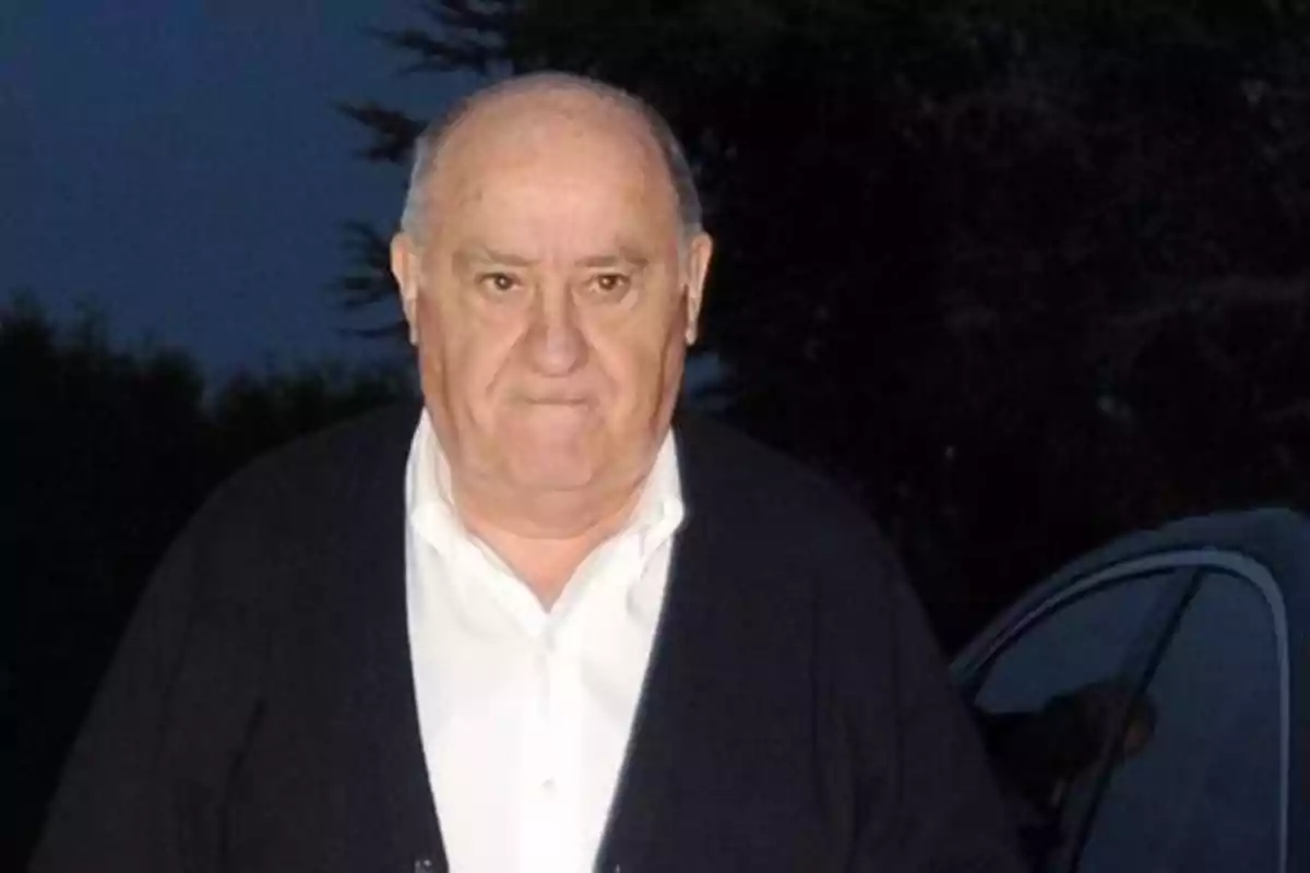 Hombre mayor calvo con suéter oscuro y camisa blanca de pie al aire libre junto a un coche al anochecer Hombre mayor calvo con suéter oscuro y camisa blanca de pie al aire libre junto a un coche al anochecer
