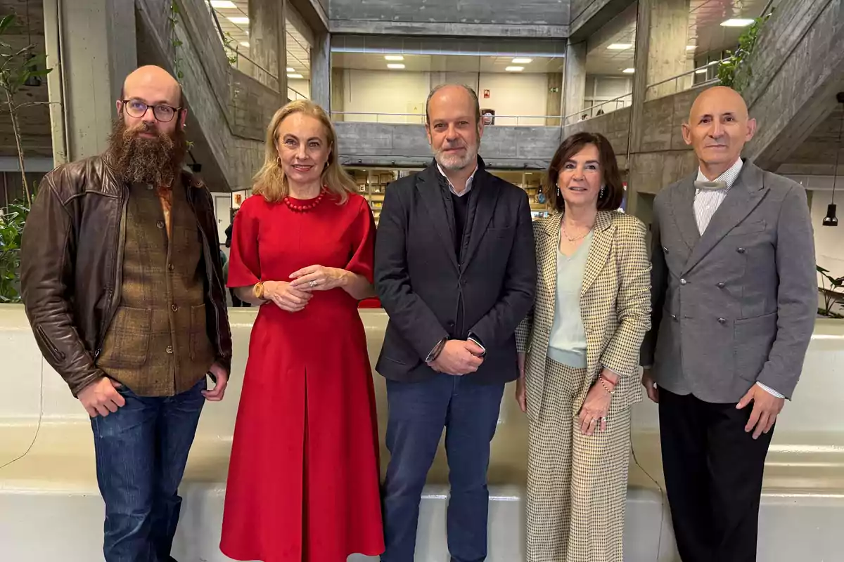 Cinco personas posan juntas en un edificio moderno con paredes de concreto y plantas alrededor.