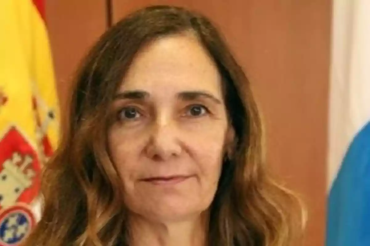 Retrato de una mujer con cabello castaño claro y ondulado, con una bandera de España en el fondo.