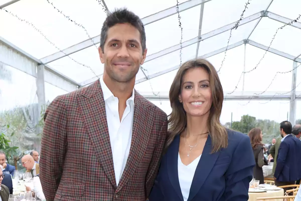 Una pareja sonriente posando en un evento bajo una carpa transparente.