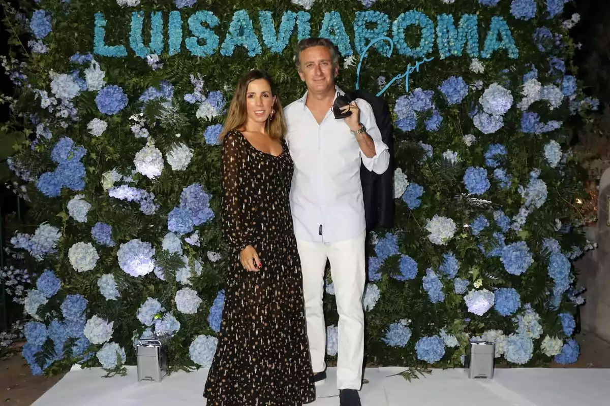 Una pareja posando frente a un fondo de flores azules y verdes con el texto 