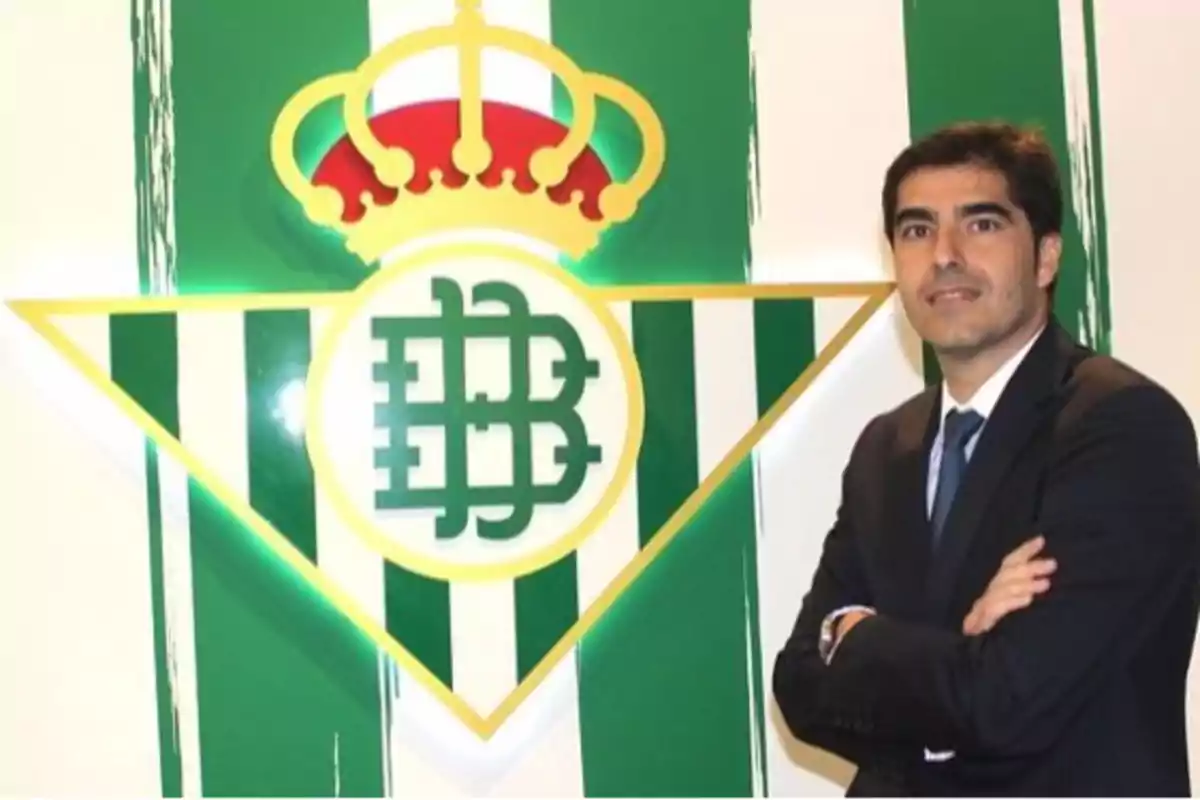 Un hombre de traje posa junto al escudo del Real Betis Balompié. Un hombre de traje posa junto al escudo del Real Betis Balompié.