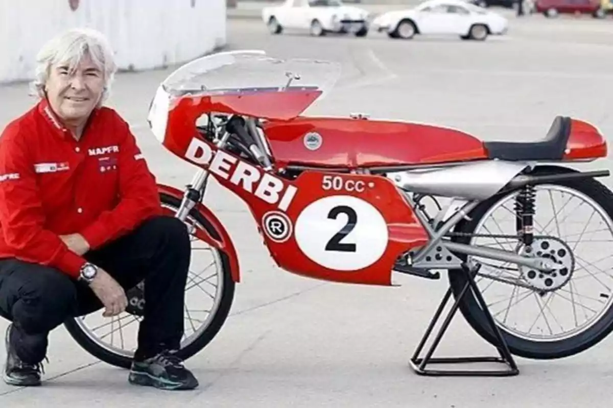 Hombre con camisa roja MAPFRE posando junto a una motocicleta roja Derbi 50 cc con el número 2 en un entorno urbano.