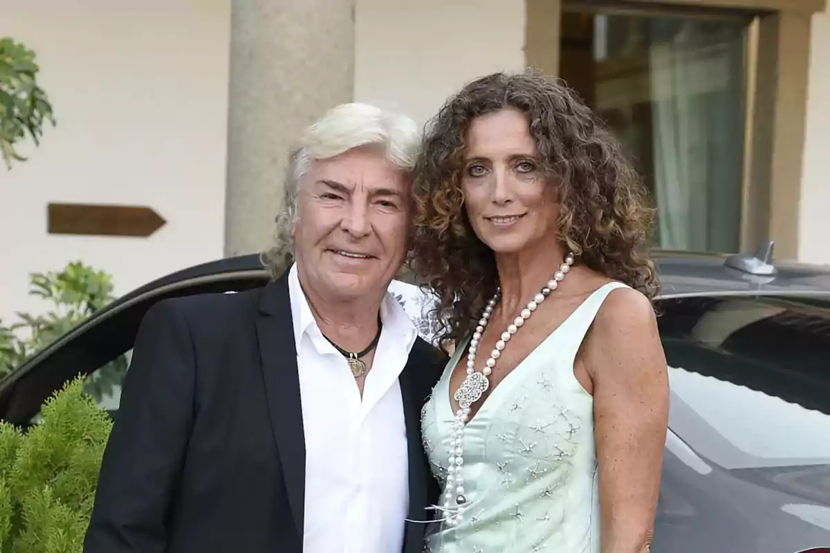 Una pareja posando juntos, el hombre lleva un traje negro y la mujer un vestido verde claro con un collar de perlas.