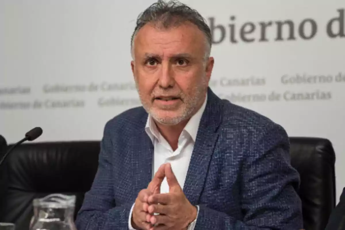 Hombre con barba y cabello canoso, vestido con un saco azul y camisa blanca, hablando en una conferencia de prensa del Gobierno de Canarias.