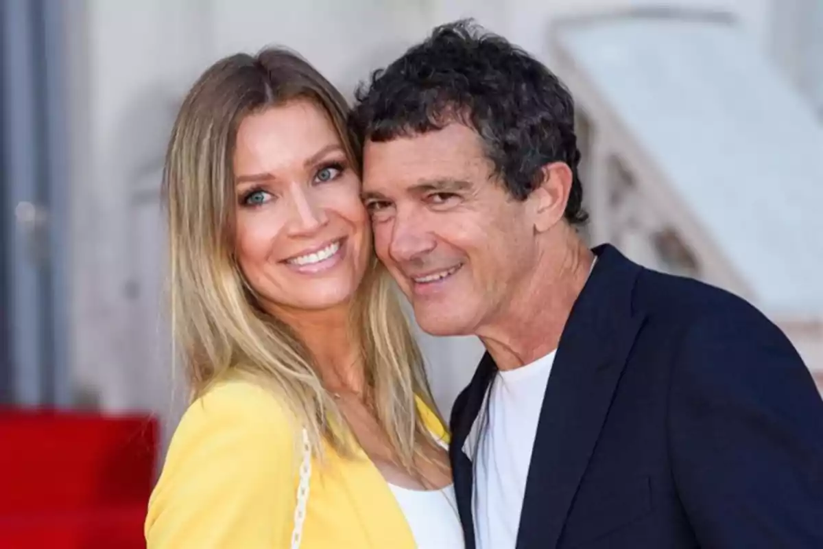 Una pareja sonriendo y posando juntos frente a una alfombra roja.