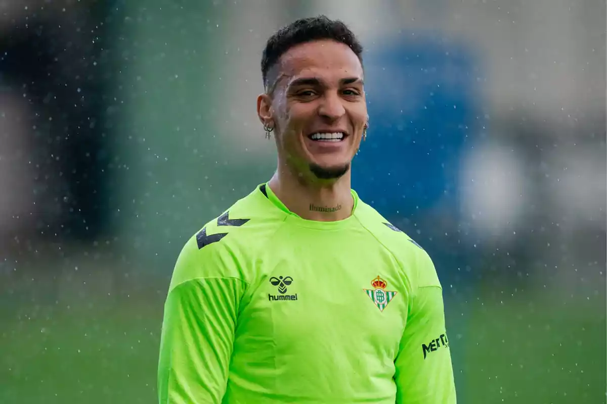 Un jugador de fútbol sonríe bajo la lluvia mientras lleva una camiseta de entrenamiento verde. Un jugador de fútbol sonríe bajo la lluvia mientras lleva una camiseta de entrenamiento verde.