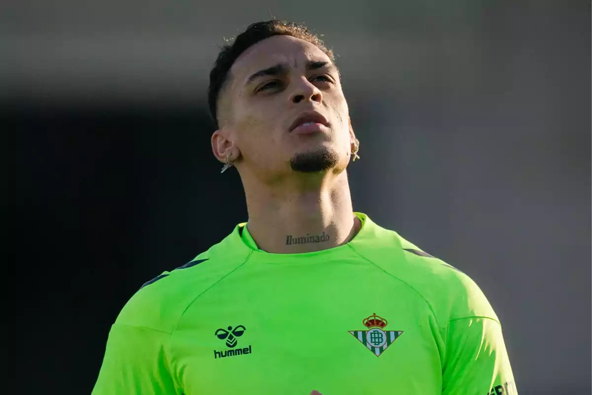 Un jugador de fútbol con camiseta verde del Real Betis mira hacia arriba con expresión pensativa. Un jugador de fútbol con camiseta verde del Real Betis mira hacia arriba con expresión pensativa.