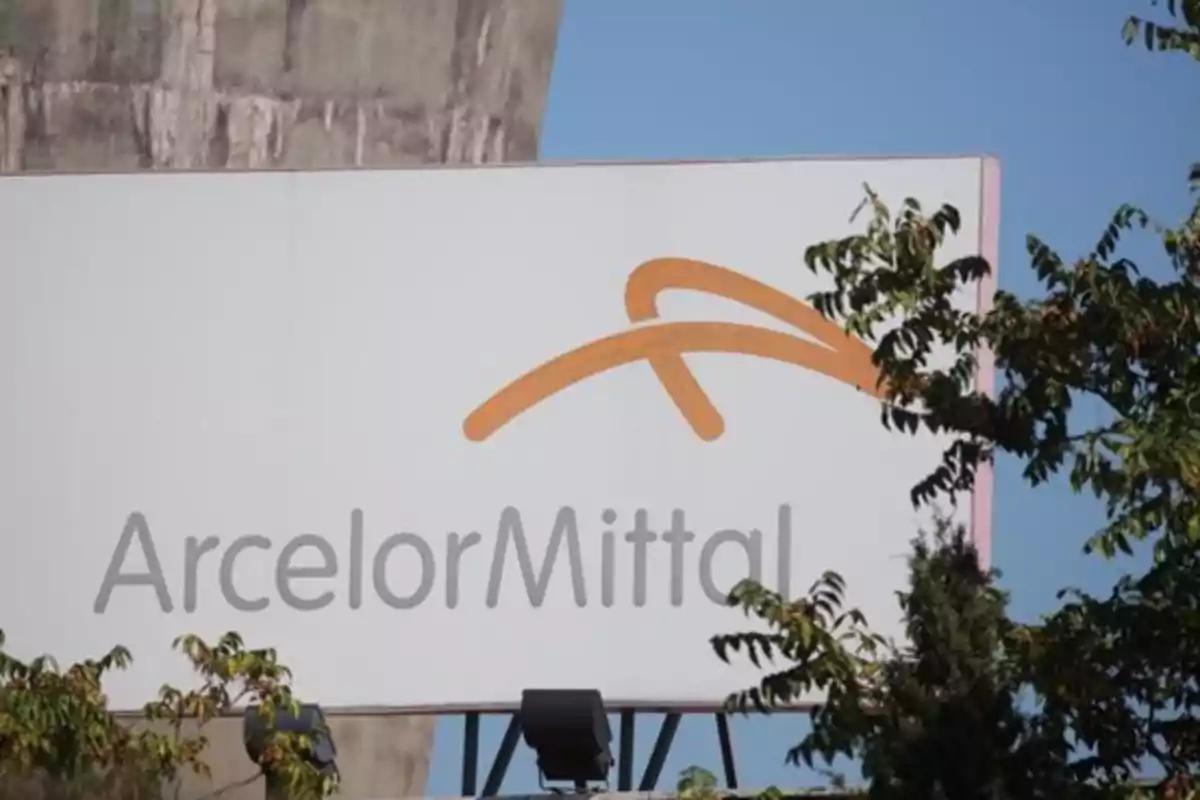 Letrero de la empresa ArcelorMittal parcialmente cubierto por ramas de árboles Letrero de la empresa ArcelorMittal parcialmente cubierto por ramas de árboles
