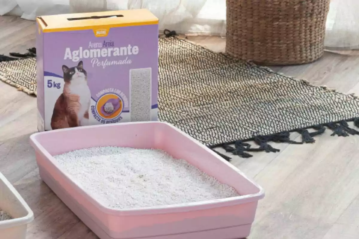 Caja de arena aglomerante para gatos junto a una bandeja sanitaria rosa con arena en el interior sobre un piso de madera y una alfombra tejida. Caja de arena aglomerante para gatos junto a una bandeja sanitaria rosa con arena en el interior sobre un piso de madera y una alfombra tejida.