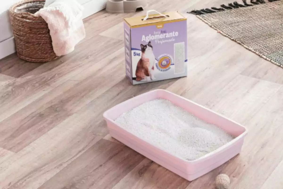 Caja de arena aglomerante para gatos junto a un arenero rosa lleno de arena sobre un suelo de madera Caja de arena aglomerante para gatos junto a un arenero rosa lleno de arena sobre un suelo de madera