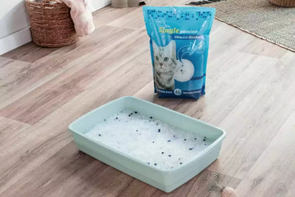 Una bandeja de arena para gatos con arena de gel de sílice en el suelo de una habitación, junto a un paquete de arena para gatos. Una bandeja de arena para gatos con arena de gel de sílice en el suelo de una habitación, junto a un paquete de arena para gatos.